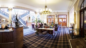 A grand lobby with a checkered floor, a central reception desk, and a staircase with ornate railings. - The Royal Highland Hotel (Inverness)