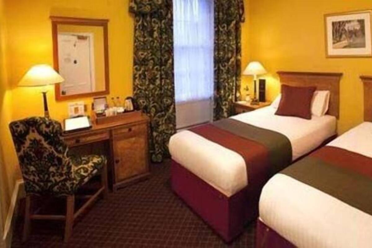 A hotel room with two beds, a desk, a chair, and a window with curtains.