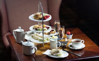 A tiered dessert tray with various pastries and fruits, a teapot, cups, and a glass of champagne on a wooden table.
