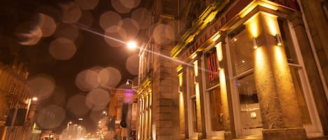 A nighttime street view with a building featuring a sign that reads "RESTAURANT ASH."