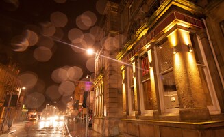 Vista nocturna de una calle con un edificio que muestra un letrero que dice 'RESTAURANT ASH'.
