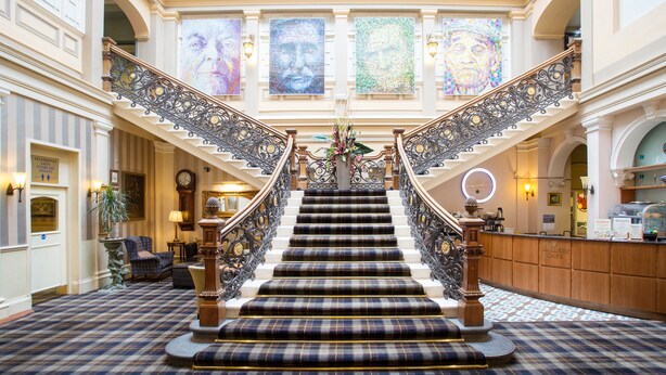 A grand staircase with ornate railings, flanked by a reception desk and a clock. - The Royal Highland Hotel (Inverness)