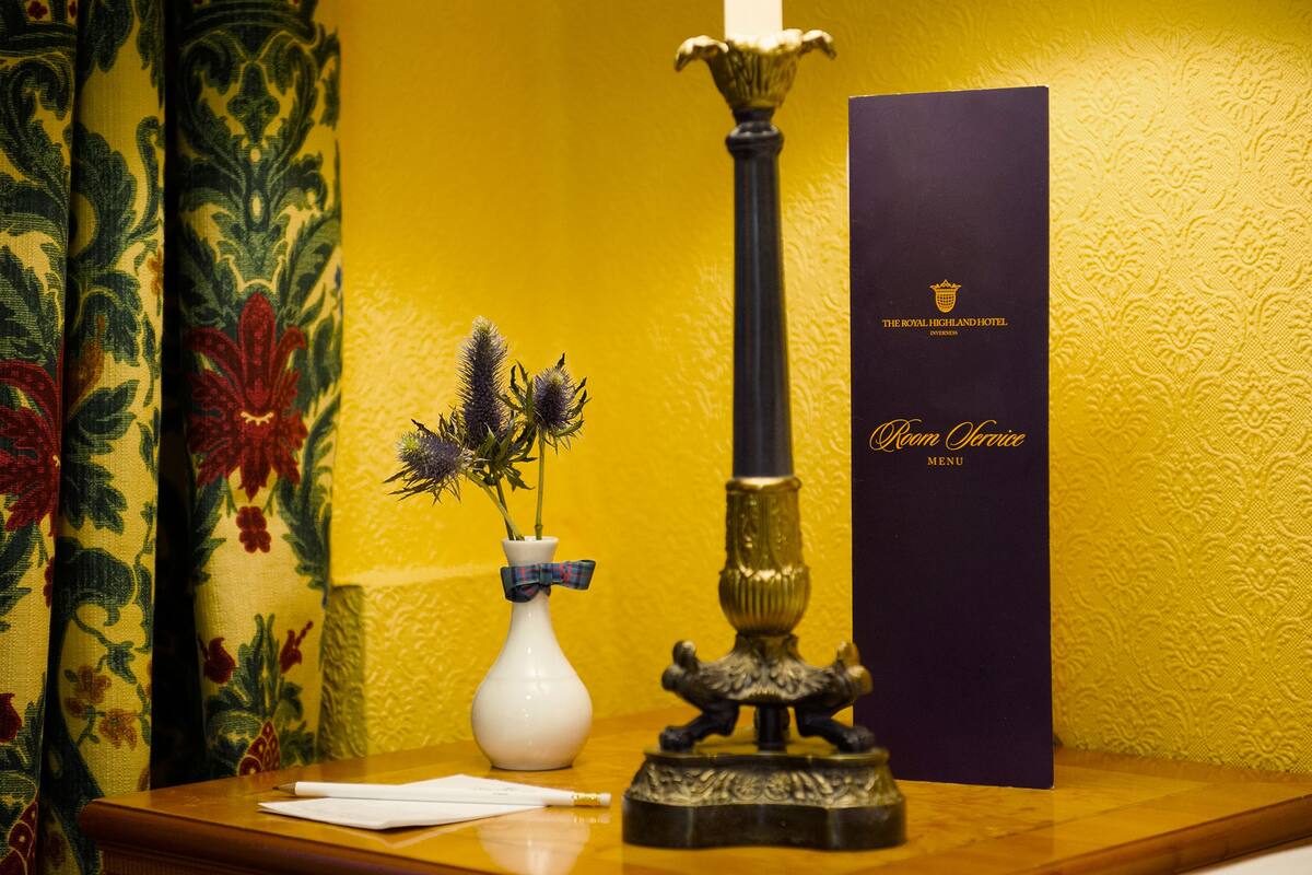 A table with a white vase containing purple flowers, a candle, and a menu from The Royal Highland Hotel.