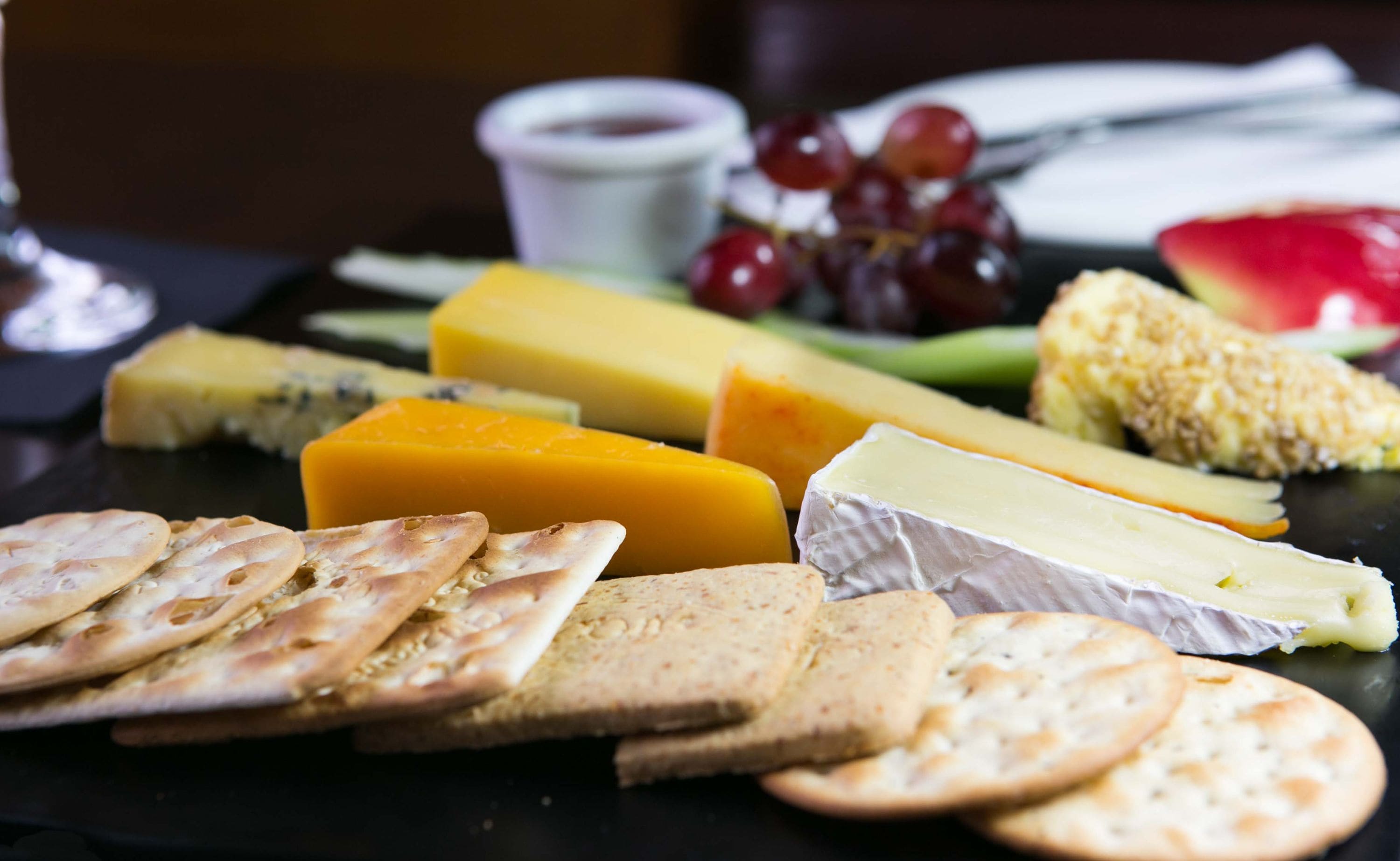 A charcuterie board with various cheeses, crackers, grapes, and a small bowl of dip.