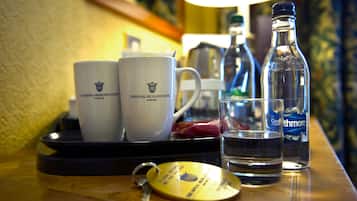 Una bandeja con dos tazas blancas, un vaso de agua, una botella de agua y un llavero con el logotipo de un hotel.