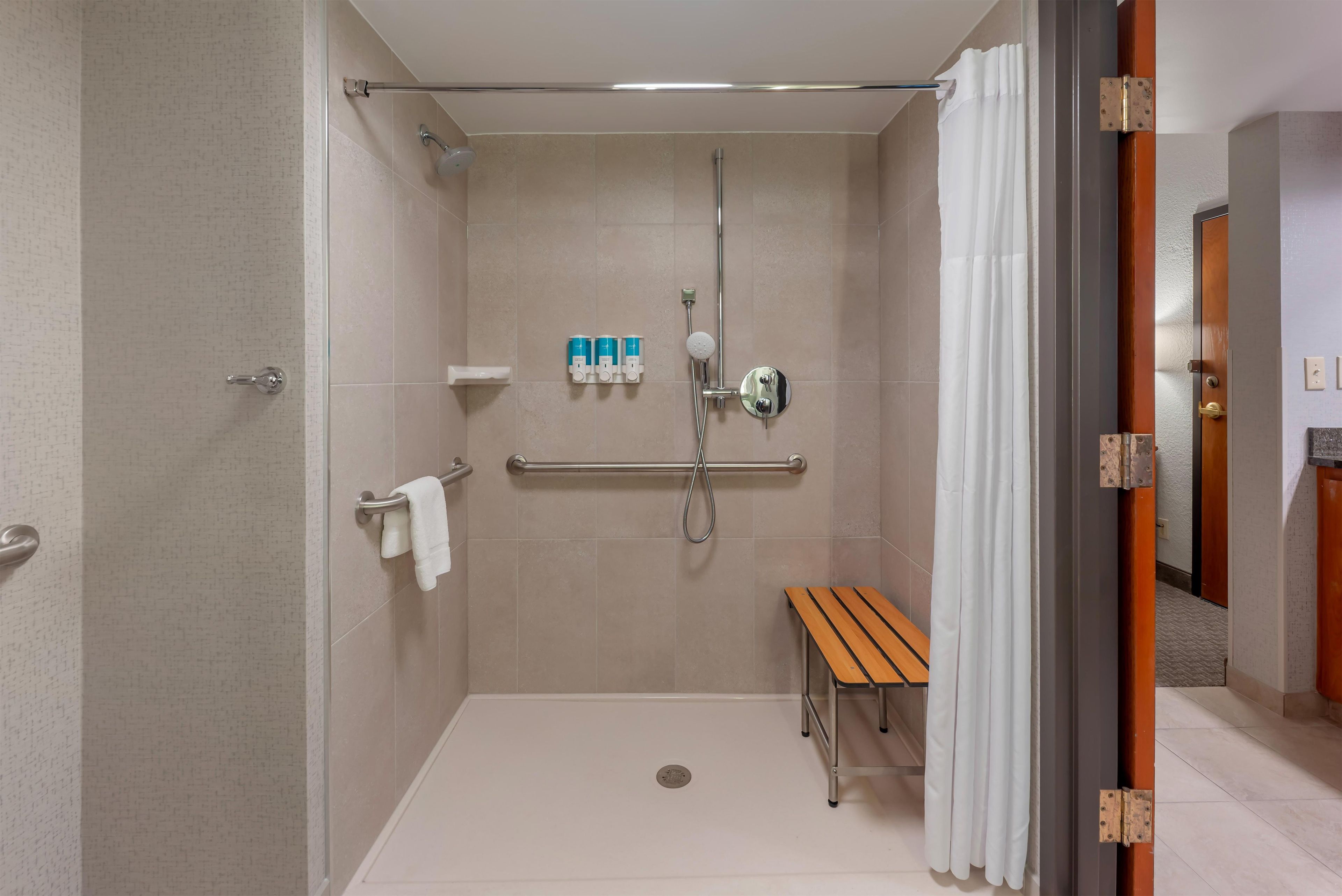 A walk-in shower with a bench, handrails, and a towel rack.