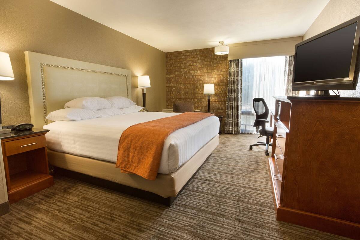 Ein Hotelzimmer mit einem großen Bett, einem Schreibtisch, einem Fernseher und einem Sessel.