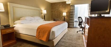 A hotel room with a large bed, a desk with a chair, a television, and a brick wall.