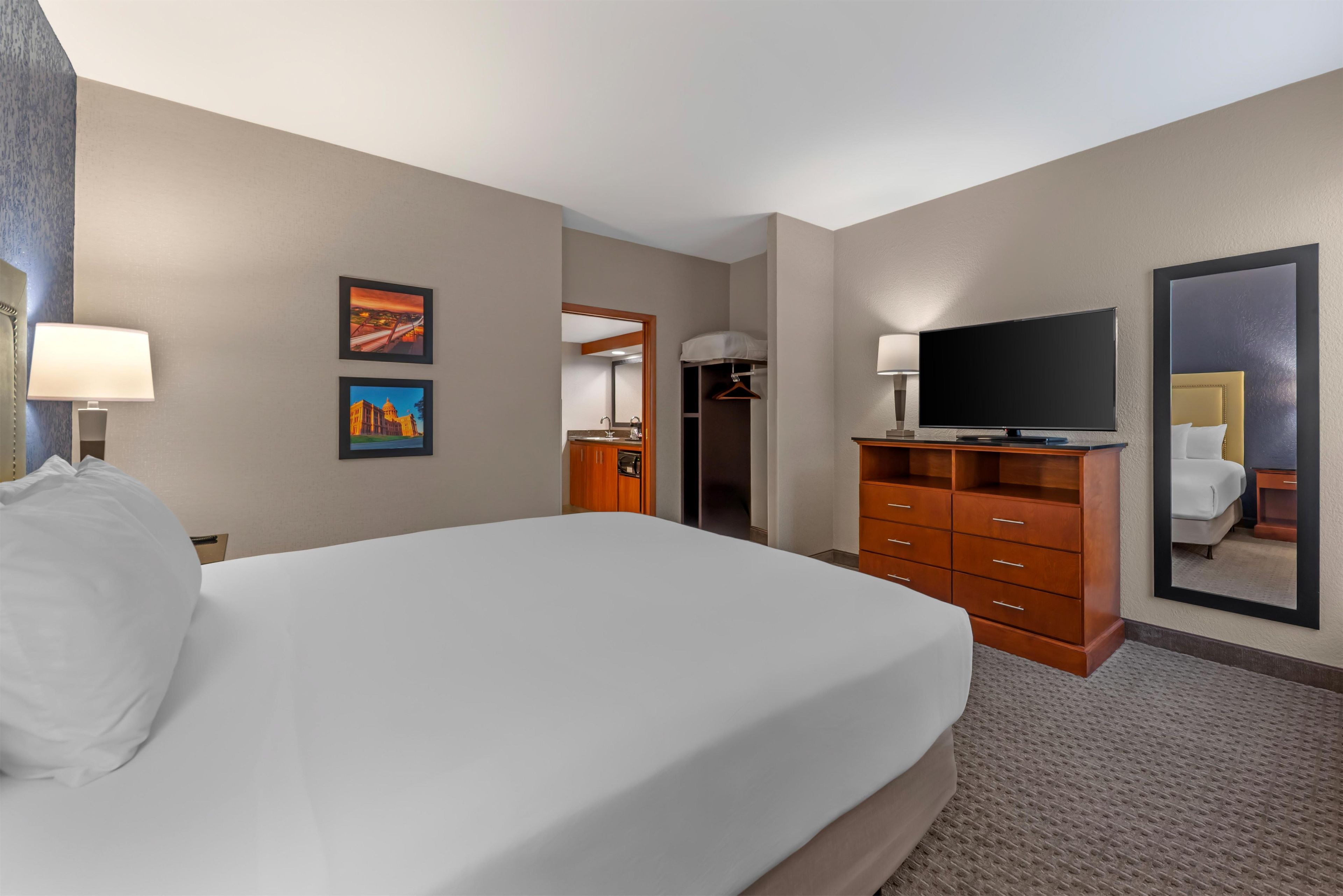 A hotel room with a large bed, a television, a dresser, and a mirror.