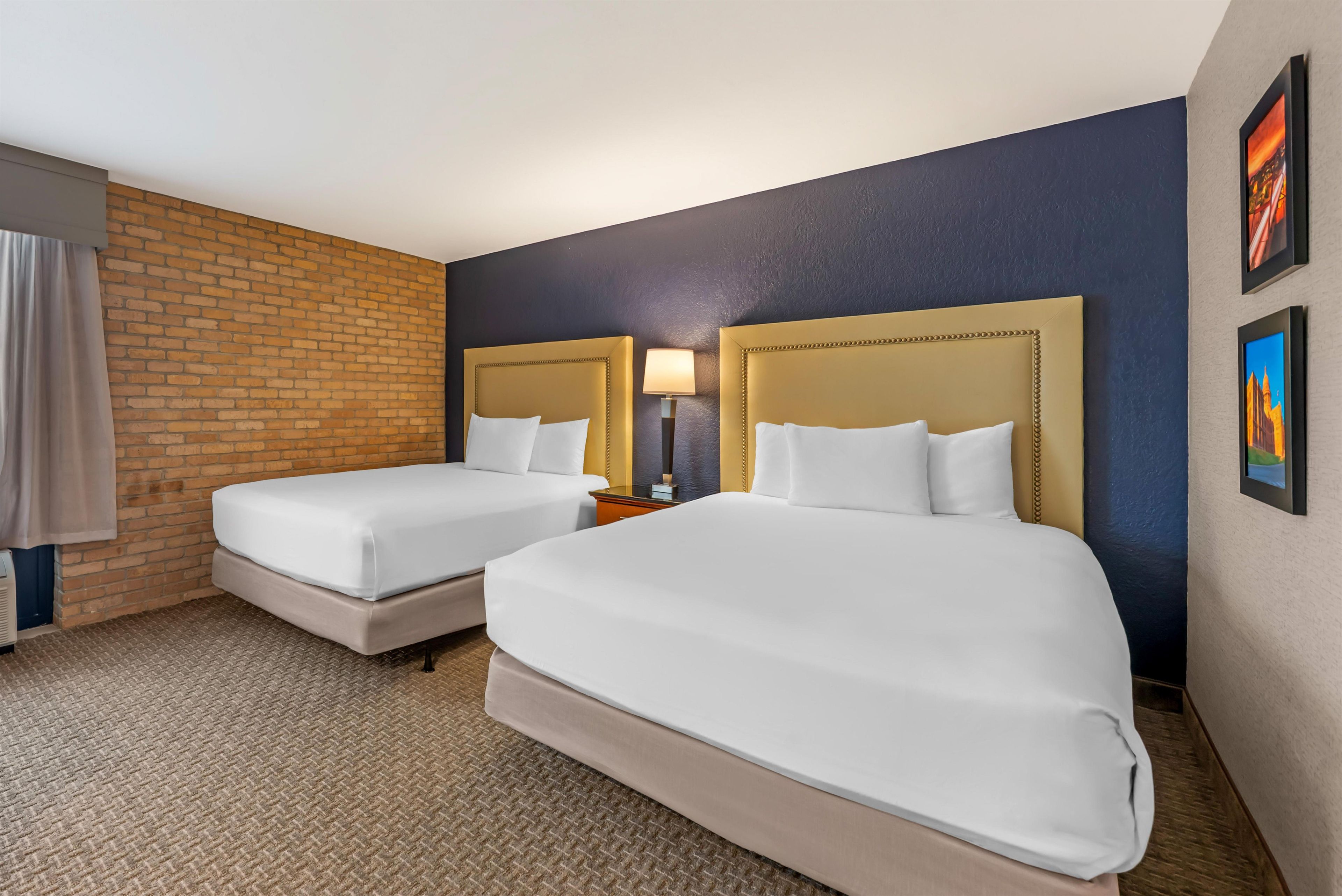 Een hotelkamer met twee bedden, een accentmuur van baksteen, een donkerblauwe wand en een vloerbedekking.