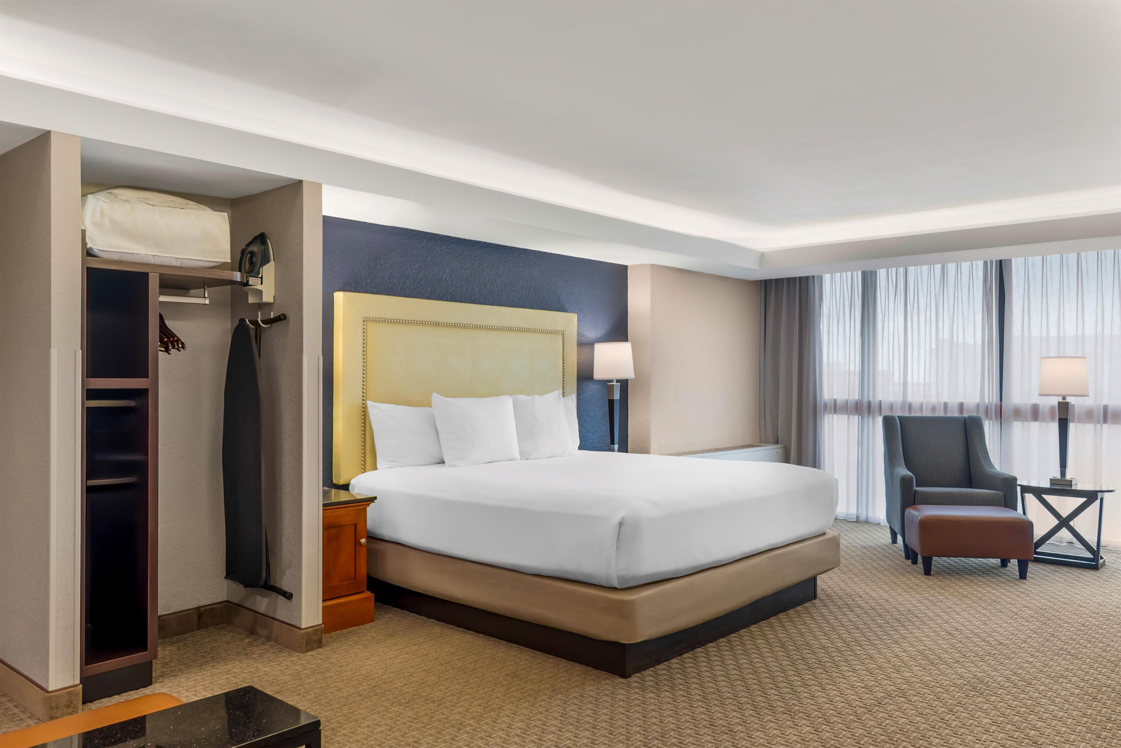 A hotel room with a bed, a chair, a desk, and a wardrobe.