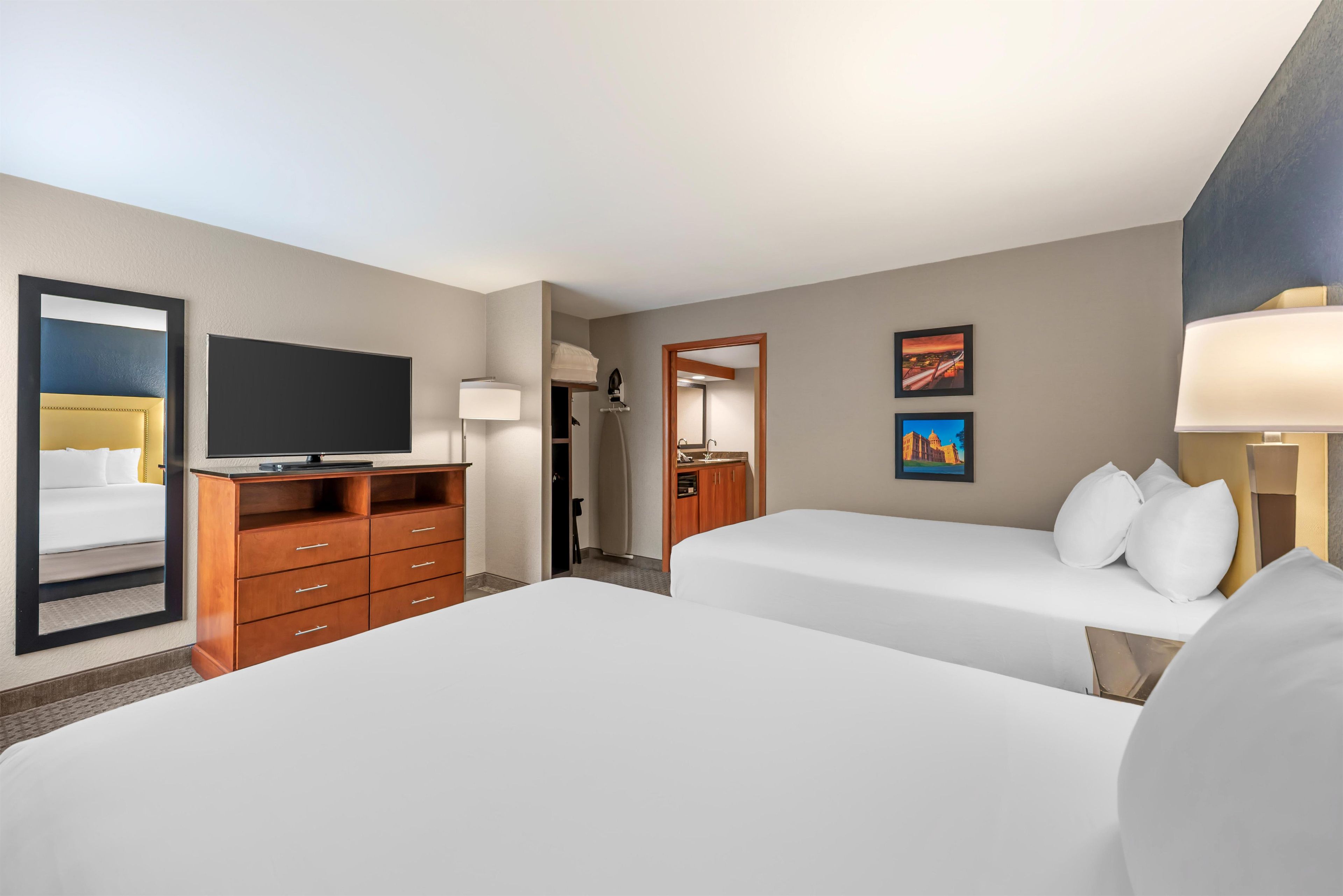 A hotel room with two beds, a TV, a dresser, a bathroom, and artwork on the walls.