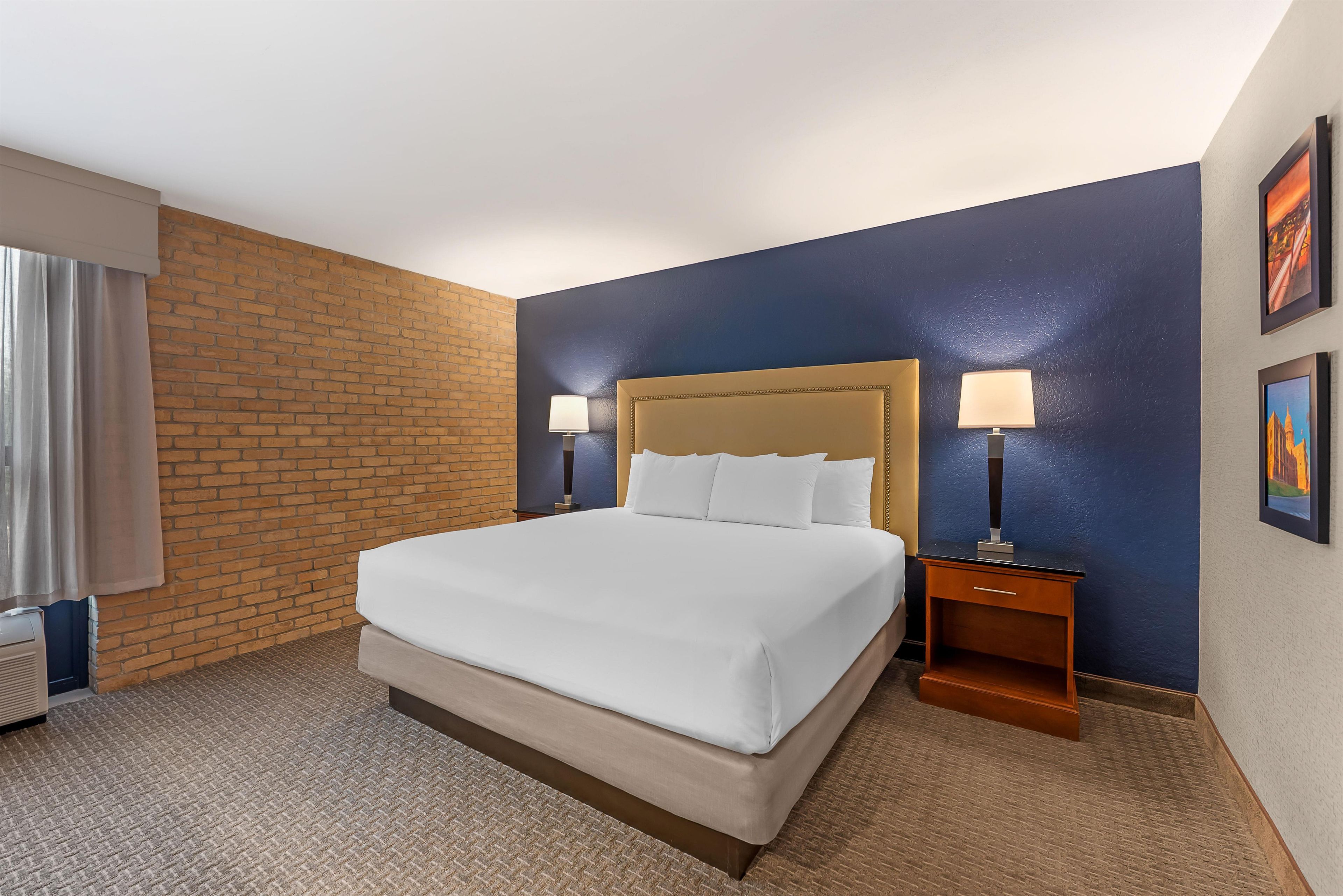 Habitación de hotel con una cama grande, dos mesitas de noche con lámparas, una pared de ladrillo decorativa y suelo alfombrado.
