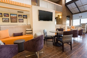 Ein moderner Lounge-Bereich mit einer Couch, Sesseln, einem Fernseher und gerahmten Bildern an der Wand.