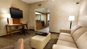A hotel room with a flat-screen TV, a desk with a chair, a sofa, an ottoman, and a lamp. - Drury Inn & Suites Austin North (Austin)