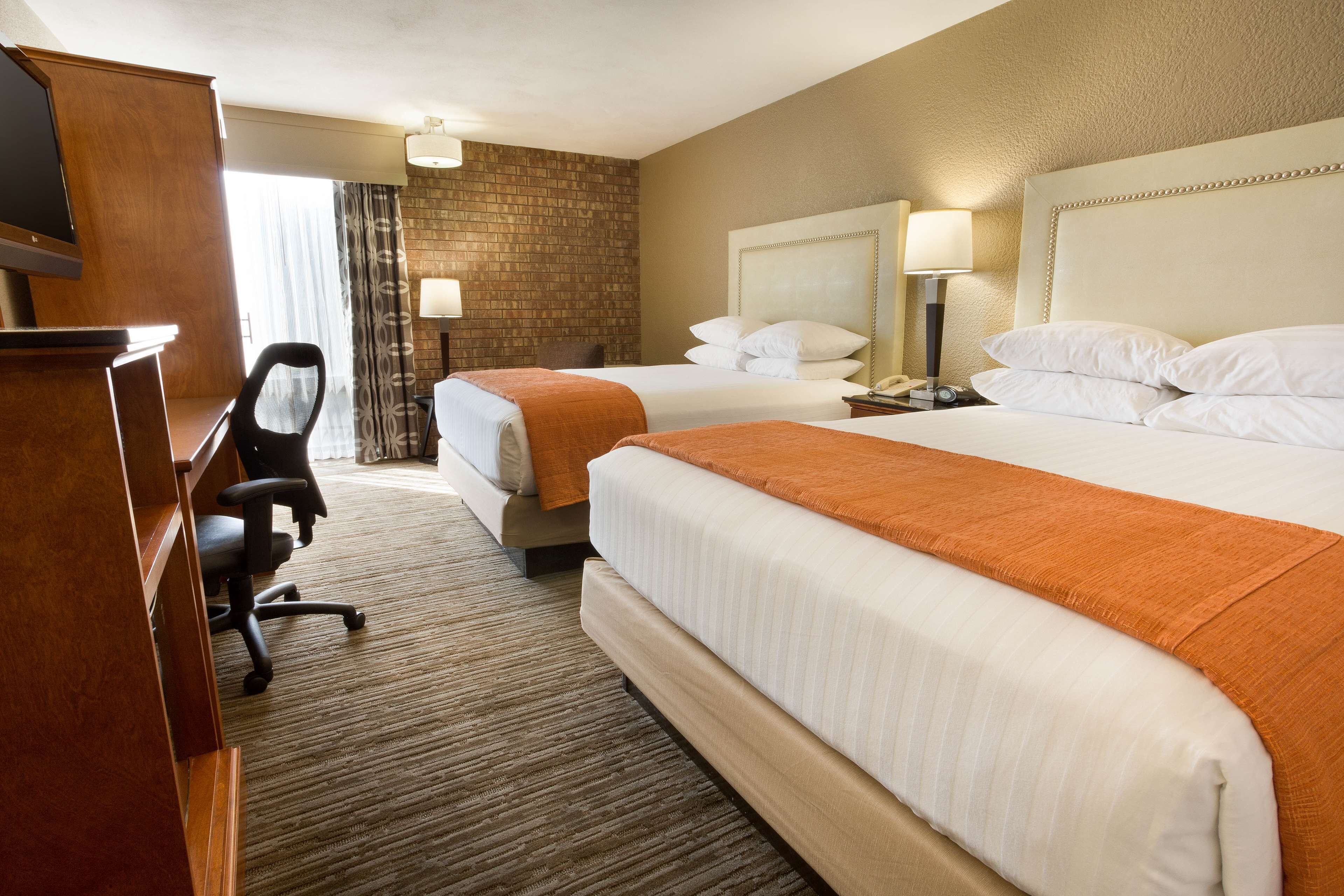 A hotel room with two beds, a desk, a chair, and a television.