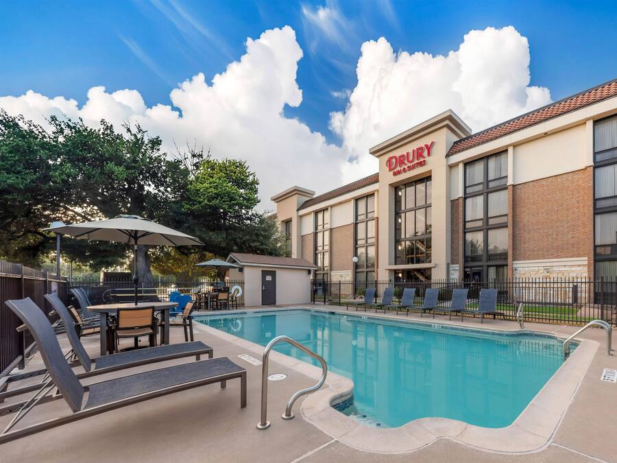 Un Drury Inn & Suites con piscina, mobiliario exterior y cielo despejado.