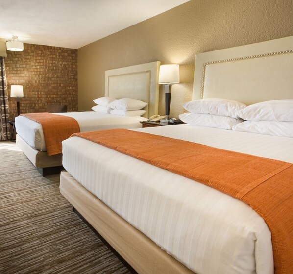 Ein Hotelzimmer mit zwei Betten, jeweils mit weißen Laken und orangefarbenen Zudecken. Nachttische mit Nachttischlampen und einer Uhr.