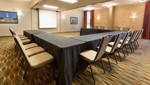 A conference room with a long table, chairs, a projector screen, and a carpeted floor.