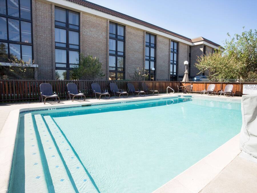 Piscina con sillas de descanso y un cartel que indica las normas de la piscina.