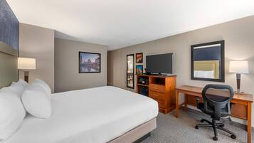 Quarto de hotel com cama, escrivaninha, cadeira, televisão e cómoda.