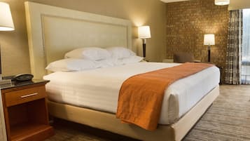 Una habitación de hotel con una cama grande, una mesita de noche, una lámpara, una silla y una pared de ladrillo.