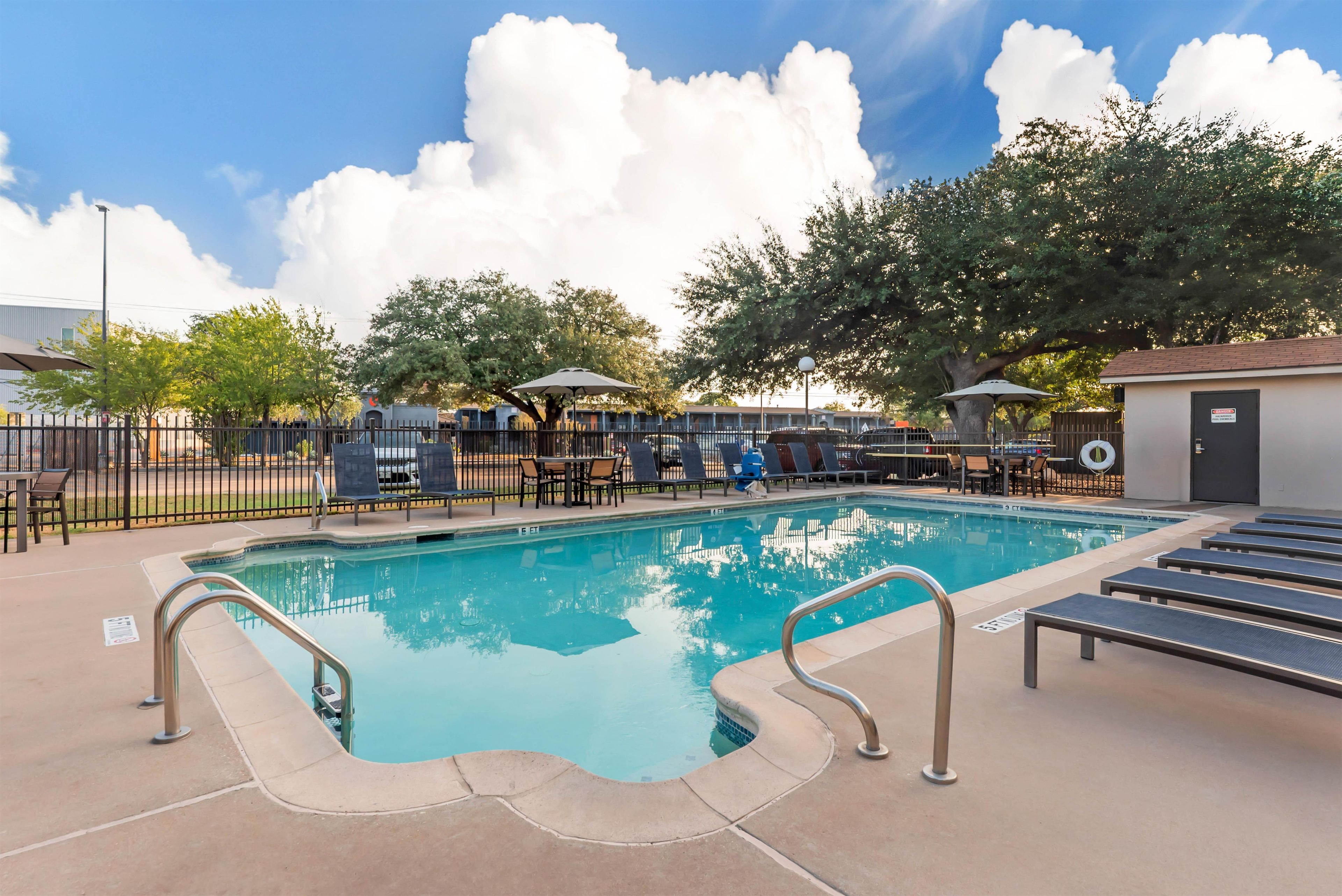 A swimming pool with lounge chairs and umbrellas, surrounded by a fence and trees.