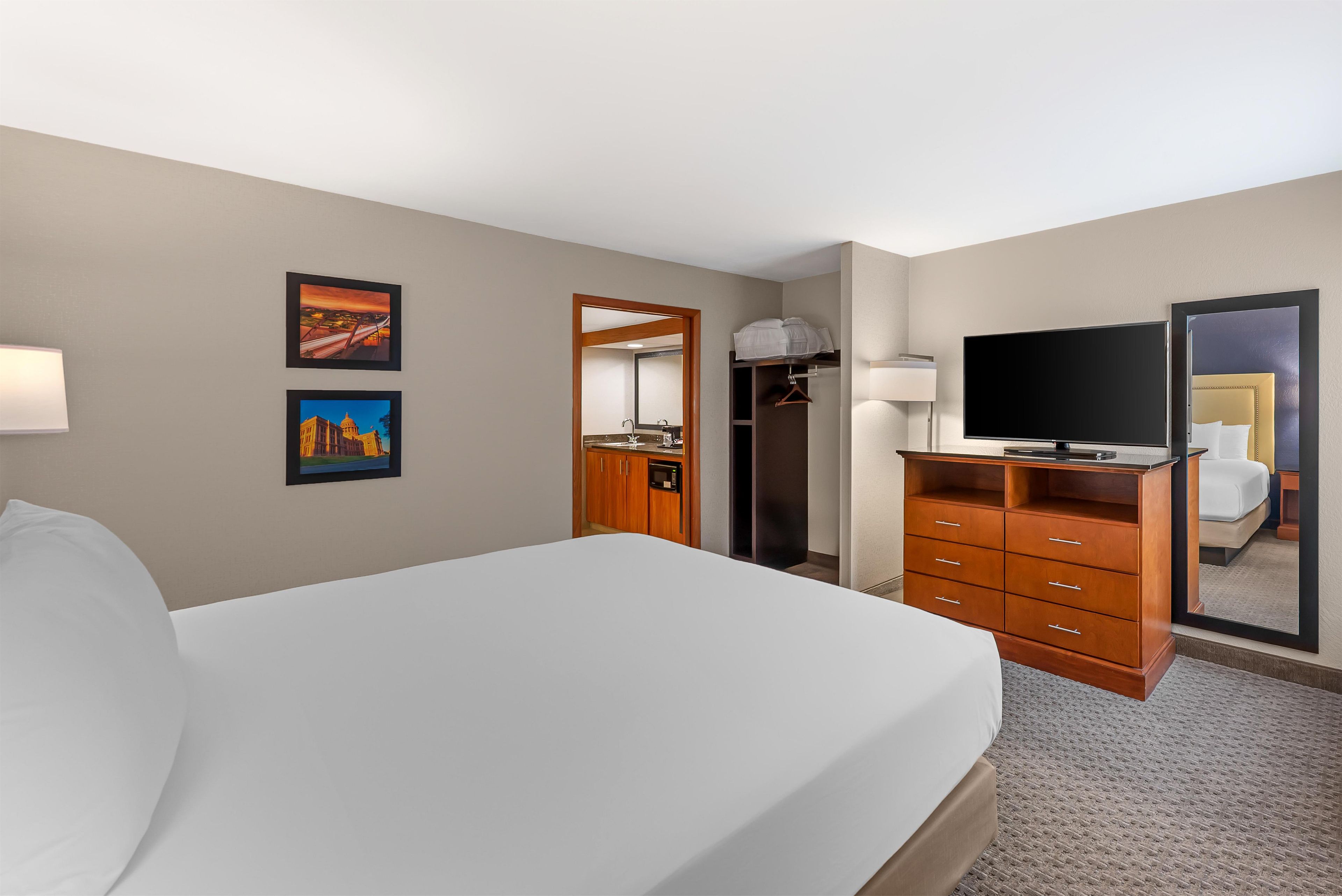 Una habitación de hotel con cama, televisión, cómoda y espejo.