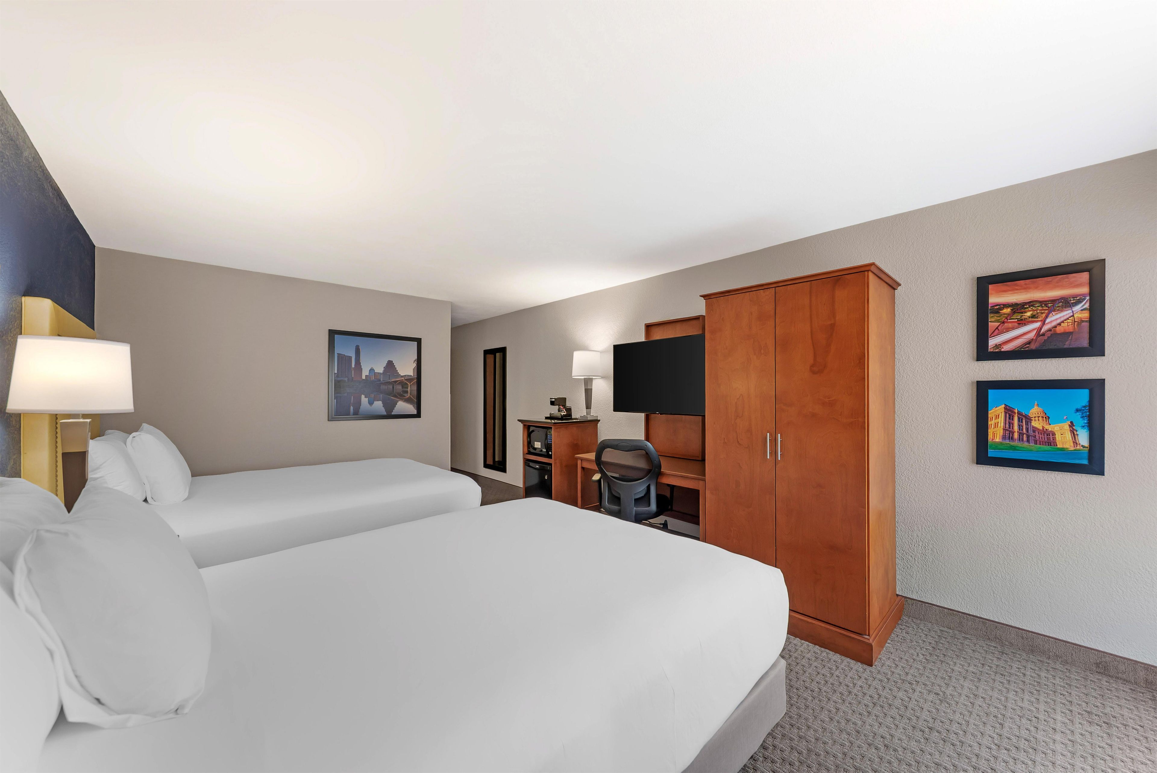 A hotel room with two beds, a desk, a chair, a TV, and two framed pictures on the wall.
