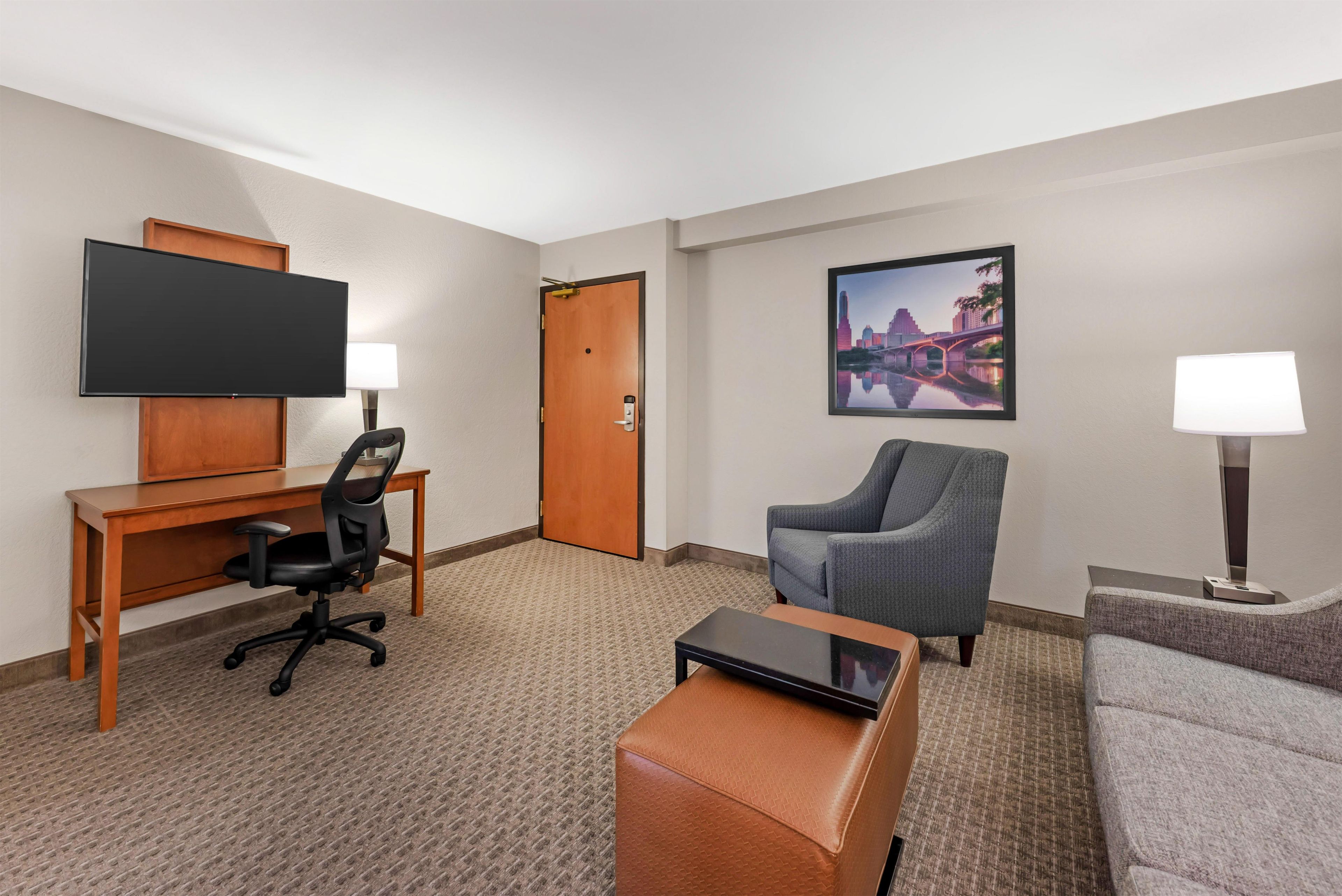 Habitación de hotel con escritorio, una silla, sofá, televisión y un cuadro en la pared.