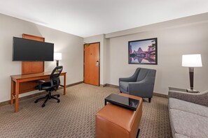 A hotel room with a desk, a chair, a sofa, a television, and a framed picture on the wall.