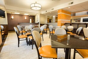 A hotel dining area with multiple tables and chairs, a large flat-screen TV, and a reception desk. - Drury Inn & Suites Austin North (Austin)