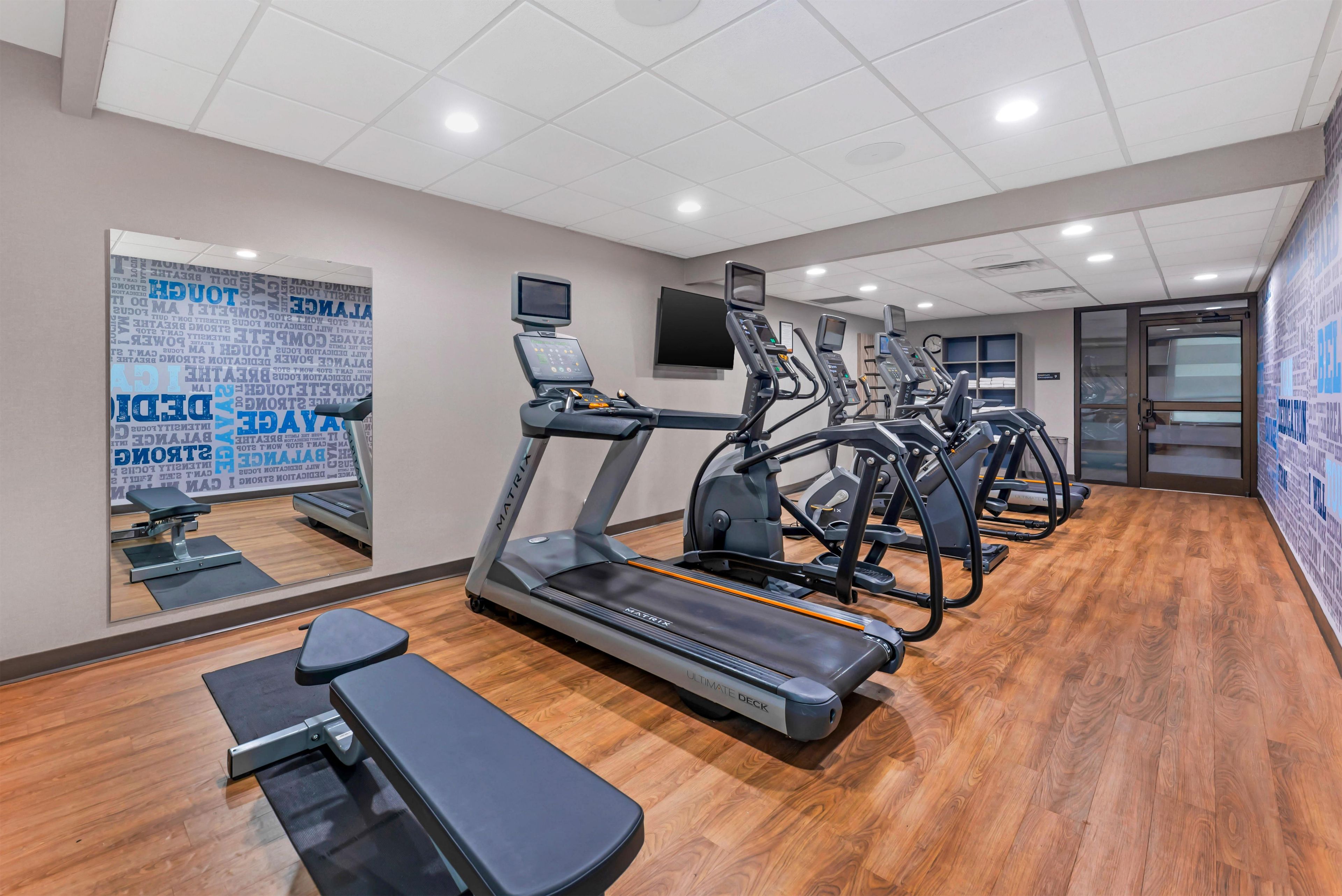 Un gimnasio con cintas de correr, una banca y un espejo con mensajes motivacionales.