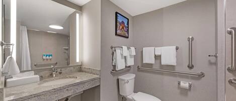 A modern bathroom with a sink, mirror, toilet, and handrails.