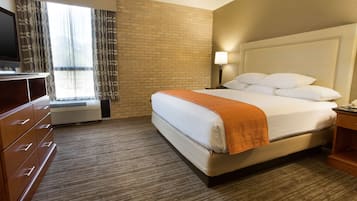 Quarto de hotel com cama, televisão, escrivaninha e janela com cortinas.