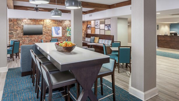 A modern hotel lobby with a stone wall, a flat-screen TV, a dining area with a long table and chairs, and a reception desk. - Hampton Inn Austin NW near The Domain (Austin)