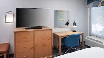 Et hotelværelse med seng, skrivebord, stol, fjernsyn, garderobeskab, skrivebordslampe og et vindue med udsigt.