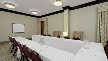 Une salle de conférence avec une longue table, des chaises, une horloge et un écran de projection.
