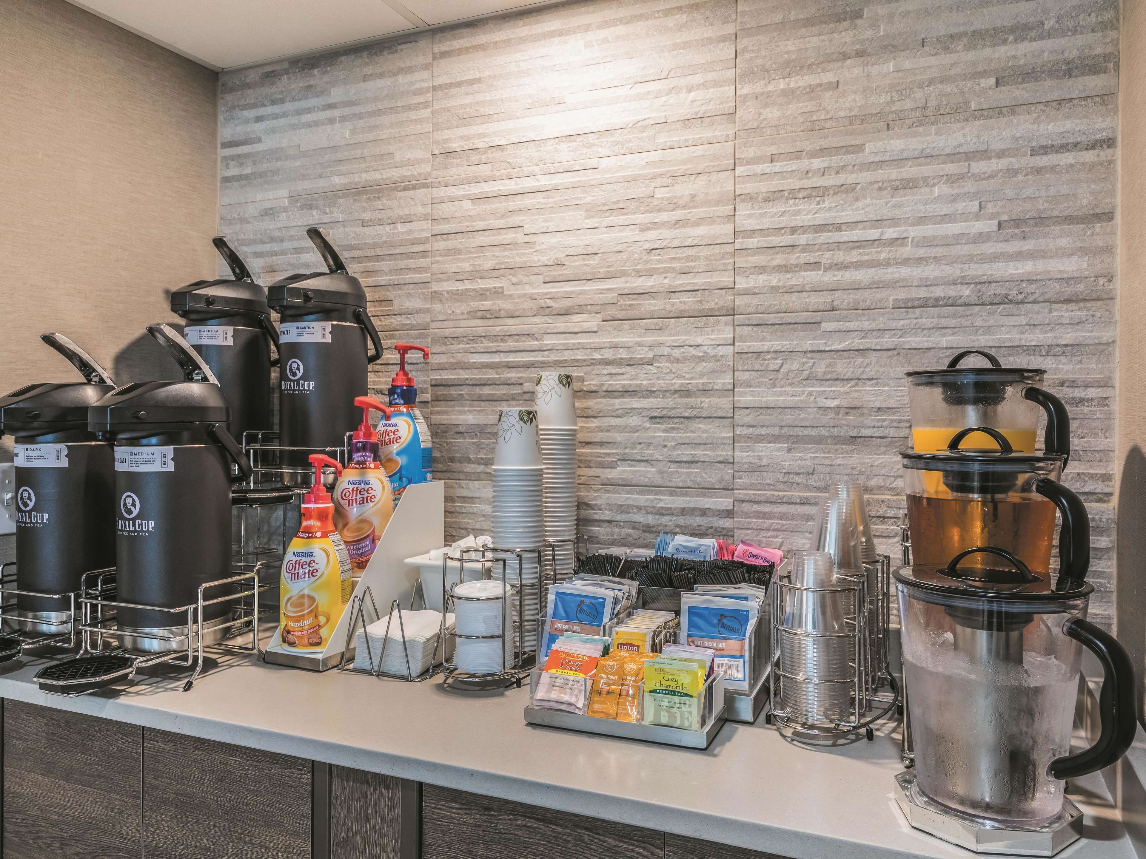 Een ontbijtbalk met koffiezetapparaten, theedispenseers en diverse koffiecups.