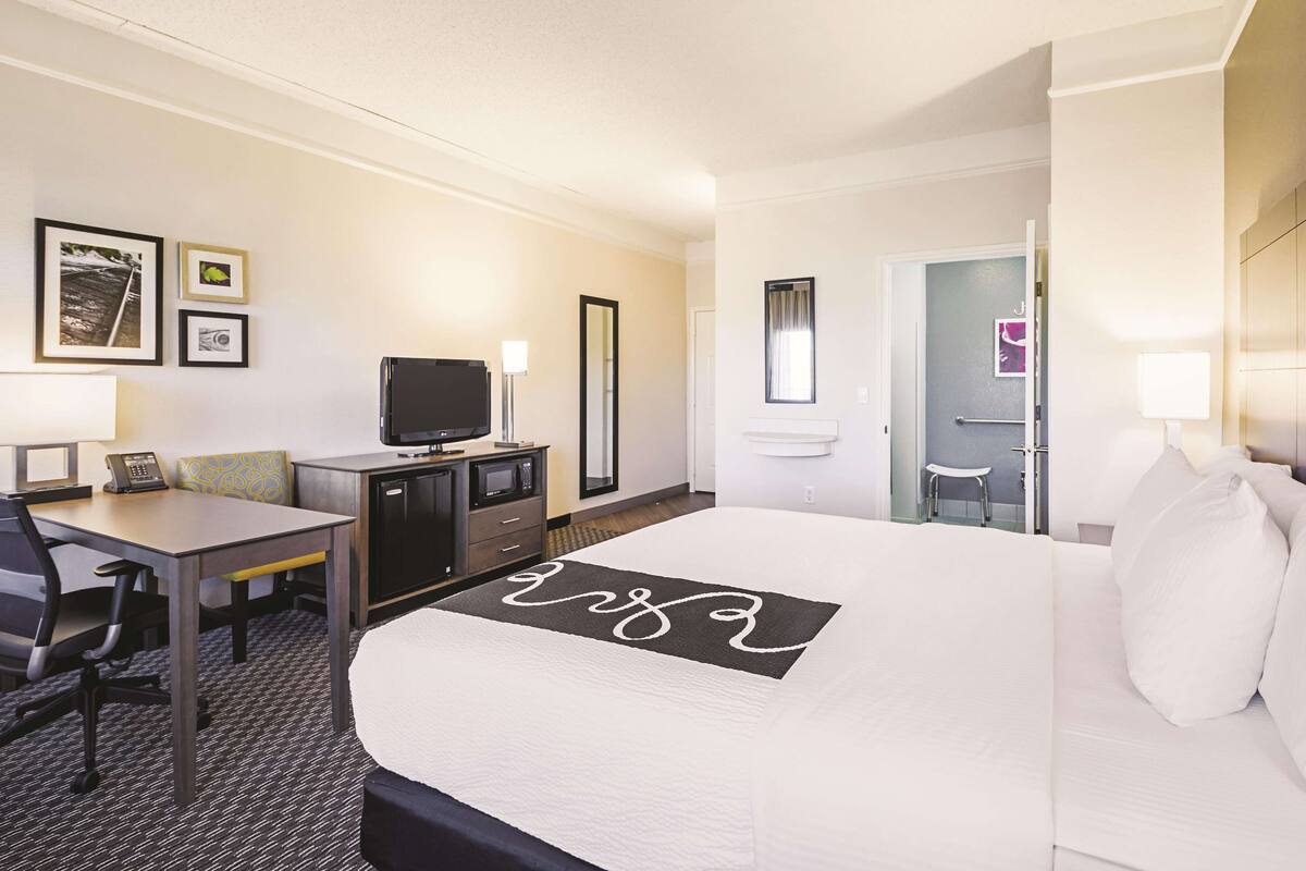 Una habitación de hotel con cama, escritorio con computadora, televisión y espejo.
