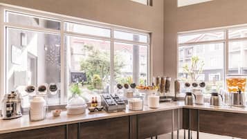 Een ontbijtbuffet met diverse drank- en etensautomaatjes, een uitzicht op buiten door grote ramen, en een modern interieur.