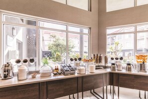 A breakfast bar with various food and drink dispensers, a view of the outside through large windows, and a modern interior design. - La Quinta Inn & Suites by Wyndham Austin Near The Domain (Austin)