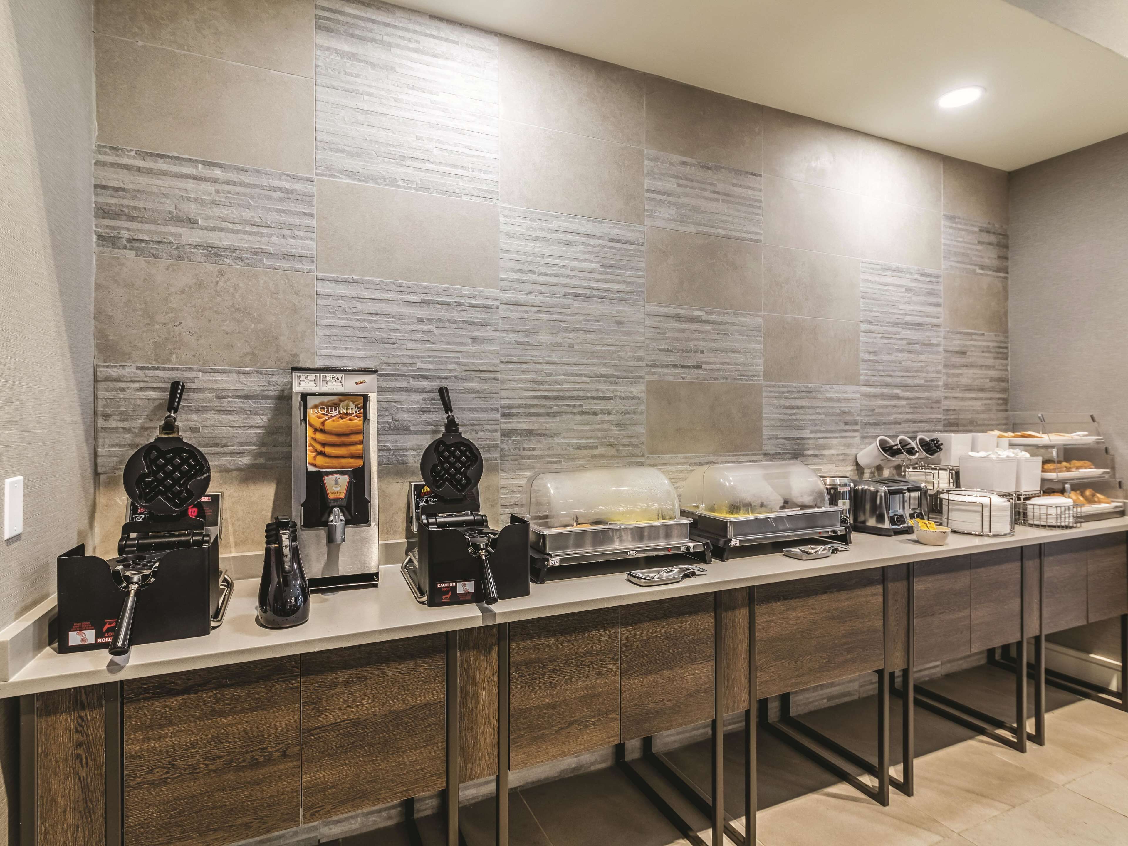 A buffet setup with waffle irons, a coffee machine, and covered food containers.