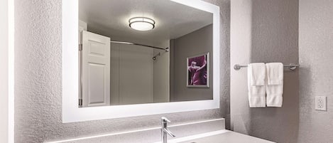Un baño con un espejo grande, un lavamanos y un perchero para toallas.