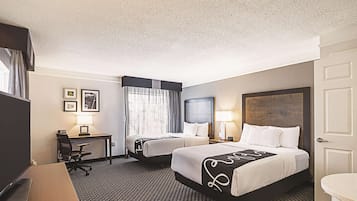 Ein Hotelzimmer mit zwei Betten, einem Schreibtisch, einem Sessel, einem Fernseher und einem Badezimmer.