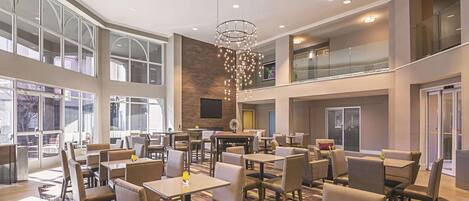 Een ruime hotellobby met verschillende zithoeken, grote ramen en een moderne kroonluchter.