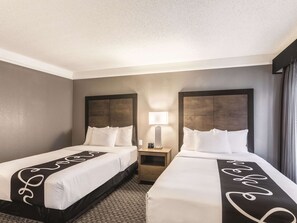 A hotel room with two beds, a nightstand with a lamp, and a view of the outside through a window. - La Quinta Inn & Suites by Wyndham Austin Near The Domain (Austin)