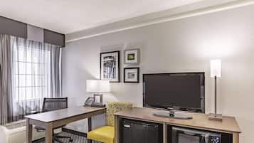 A hotel room with a desk, chair, television, mini-fridge, microwave, and a window with curtains.