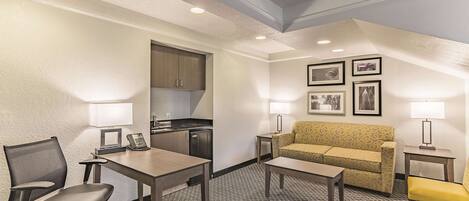 A hotel room with a kitchenette, a sofa, a dining table, and a chair.