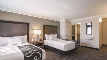 A hotel room with two beds, a nightstand with a lamp, a door leading to another room, and a small window.